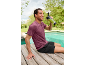 Homem de t-shirt desportiva e calções a beber um batido verde junto à piscina.