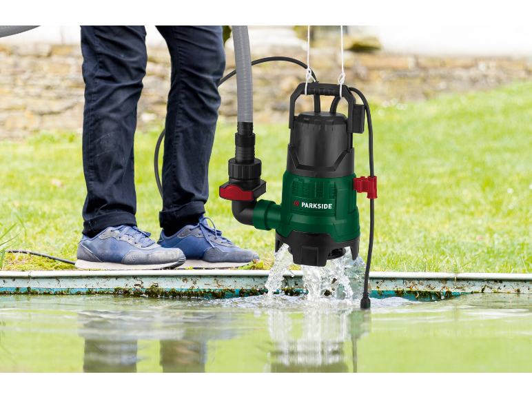 Bomba de água submersível verde e preta com mangueira, usada por uma pessoa para drenar água.
