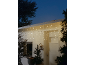 Luzes de corda tipo cascata numa cabana de madeira branca, decorada para o Natal