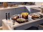 Panelas e frigideiras de cobre numa placa de indução, com comida e acessórios de cozinha.