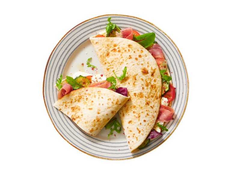 Piadina com presunto, mozzarella, tomate, curgete e rúcula num prato listrado.