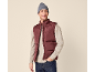Homem sorridente com colete acolchoado bordô, camisola bege e gorro cinzento.