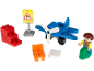 Avião de brinquedo, figura de piloto, blocos vermelhos, sinal de biruta, cadeira laranja e bloco branco.