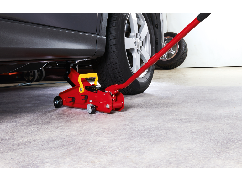 Macaco hidráulico vermelho debaixo de um carro numa garagem.