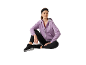 Mulher sentada, vestindo um casaco lilás com zíper, leggings pretas e tênis.