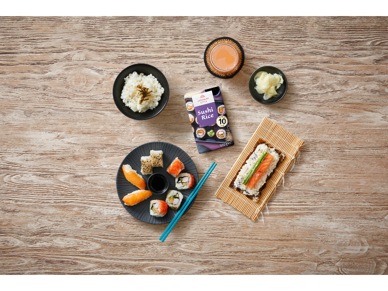 Arroz para sushi, sushi variado, gengibre e bebida em madeira clara.