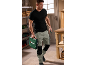 Homem com roupa de trabalho a carregar uma caixa de ferramentas verde e uma ferramenta manual.