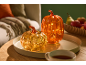 Duas abóboras decorativas iluminadas numa bandeja, com uma sala de estar acolhedora ao fundo.