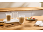 Lattes em copos de parede dupla com macarons e açúcar mascavo em uma mesa de madeira.