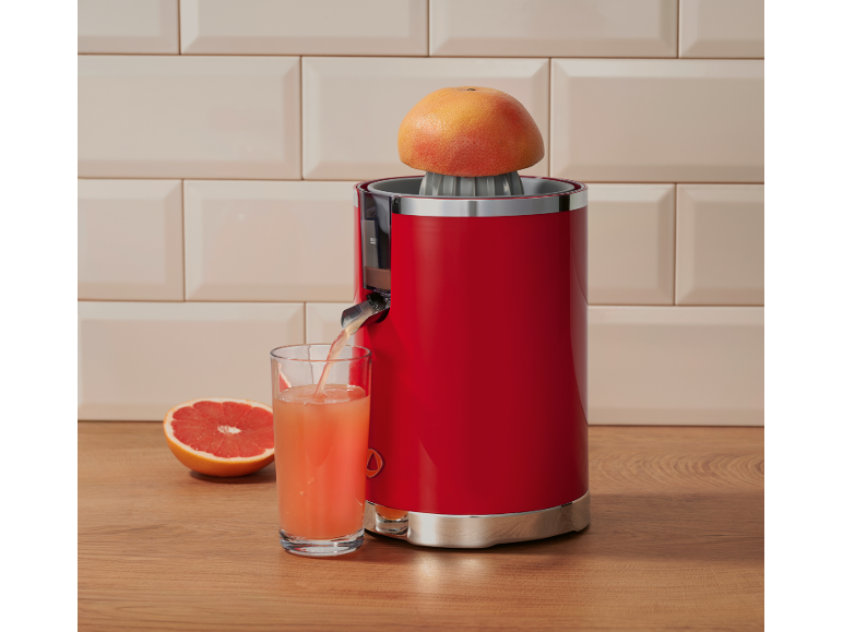Espremedor de citrinos vermelho com uma toranja espremida e um copo de sumo numa bancada de madeira.
