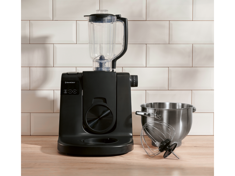 Robô de cozinha preto com liquidificador, taça de aço inoxidável e batedor numa superfície de madeira.