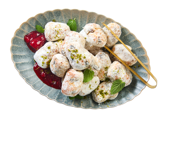 Biscoitos de Natal açucarados com pistácios, hortelã e geleia de framboesa num prato.