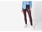 Mulher com camisa jeans azul e leggings de couro sintético bordô, com tênis brancos.