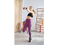 Mulher de leggings roxos e sutiã desportivo preto com halteres num ginásio.