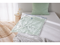 Saco de armazenamento a vácuo com roupa verde sobre uma cama branca, com almofada e cobertor.