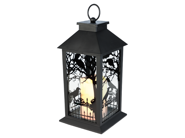 Lanterna decorativa preta com silhuetas de corvos e árvores, iluminada por uma vela.