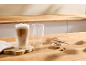 Dois copos de latte macchiato, um cheio, o outro vazio, com biscoitos numa mesa de madeira.