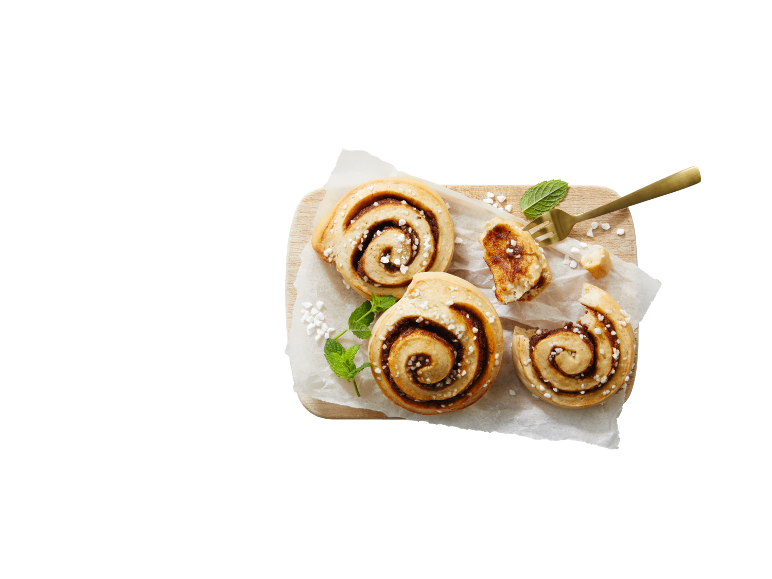 Pãezinhos de canela numa tábua de madeira com papel vegetal, guarnecidos com hortelã e açúcar.