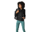 Mulher sorridente com casaco preto e leggings desportivas verde-água, mochila cinzenta.
