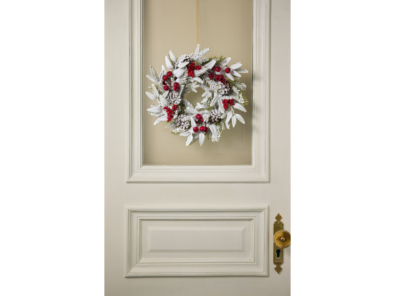 Coroa de Natal flocada com bagas vermelhas e pinhas numa porta.