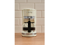 Máquina de café retro creme com jarra de vidro cheia de café numa bancada de madeira.