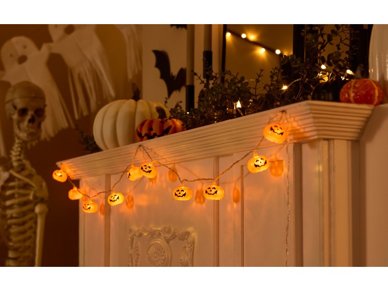 Decorações de Halloween com abóboras luminosas, um esqueleto e fantasmas de papel.