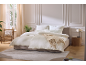 Quarto acolhedor com cama branca, mesa de cabeceira e poltrona junto à janela.
