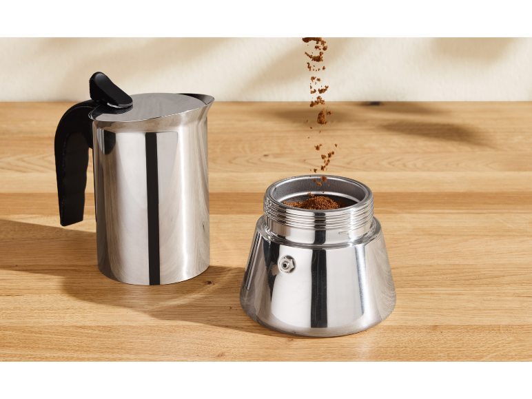 Máquina de café com café moído sobre uma mesa de madeira.