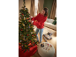 Mulher a decorar uma árvore de Natal com luzes e ornamentos, ao lado de presentes embrulhados.