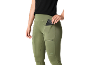 Mulher de leggings verdes com bolsos laterais, um com um telemóvel.