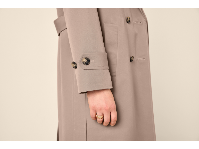 Mulher com gabardine bege e anel dourado na mão.