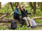 Dois caminhantes com casacos e calças desportivas, sentados num tronco de árvore com mochilas e bastões.