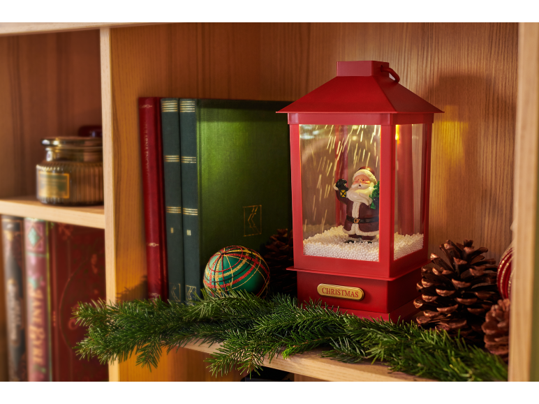 Decoração de Natal com lanterna vermelha com Pai Natal, livros e guirlanda numa prateleira de madeira.