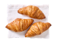 Três croissants dourados sobre um guardanapo de linho branco.