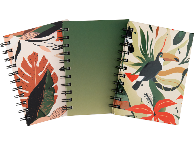 Três cadernos de argolas, dois com padrões de folhas tropicais e pássaros, um verde.