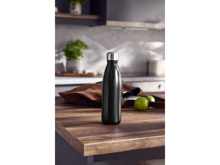 Garrafa térmica preta sobre uma mesa de cozinha, com limas verdes e tecido castanho.