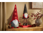 Dois gnomos festivos com chapéus iluminados e um vaso de bagas vermelhas numa superfície de madeira.