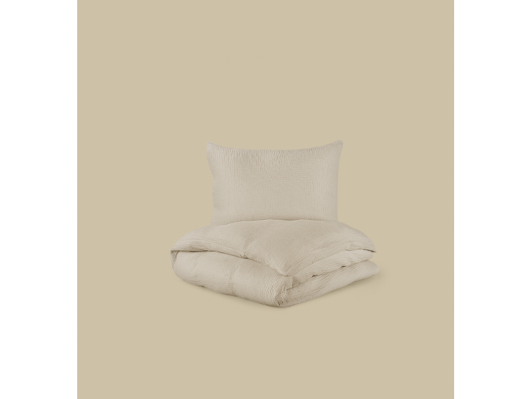 Conjunto de roupa de cama de algodão bege claro, com uma almofada e um edredão dobrado.