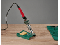 Ferro de soldar com suporte e esponja, e tapete de silicone numa mesa de madeira.
