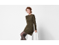 Mulher com vestido de malha verde-oliva e meias pretas, sentada num banco branco.