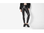 Mulher com leggings de couro pretas, casaco preto e mocassins com fivela.