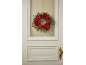 Grinalda de Natal vermelha e verde pendurada numa porta branca com maçaneta dourada.