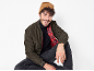 Homem com gorro castanho, casaco bomber verde-oliva, gola alta preta e jeans escuros.