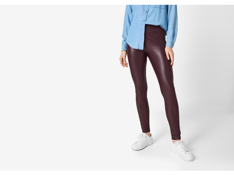 Mulher com camisa jeans azul e leggings de couro sintético bordô, com tênis brancos.