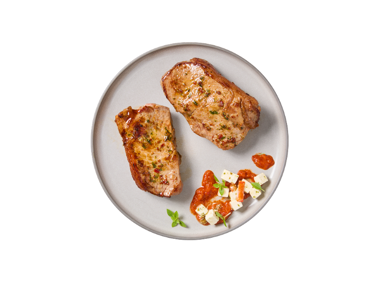 Dois bifes de porco fritos com molho de tomate e queijo feta num prato.
