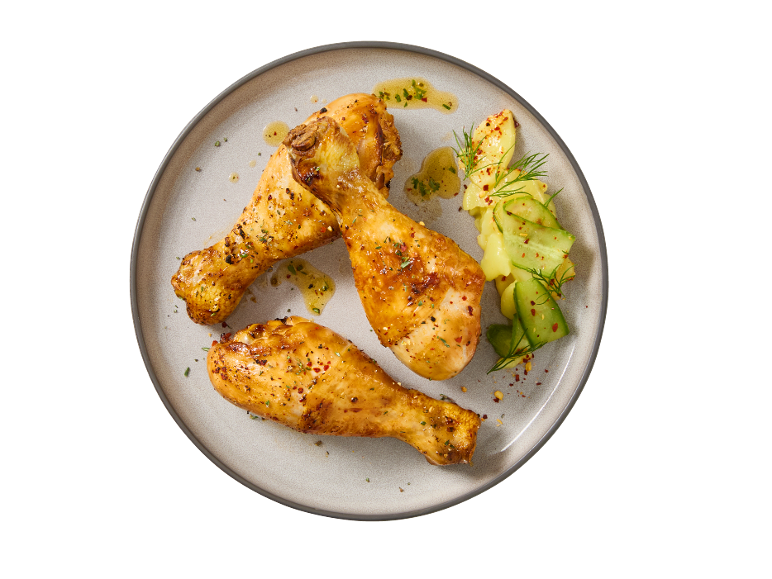 Três coxas de frango assadas com salada de batata e pepino num prato.