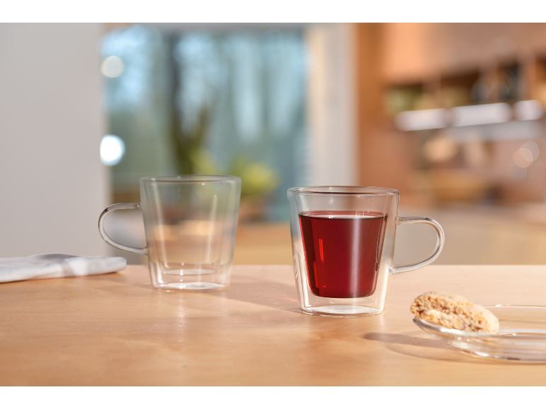 Duas canecas de vidro, uma com chá vermelho, sobre uma mesa de madeira com um biscoito.