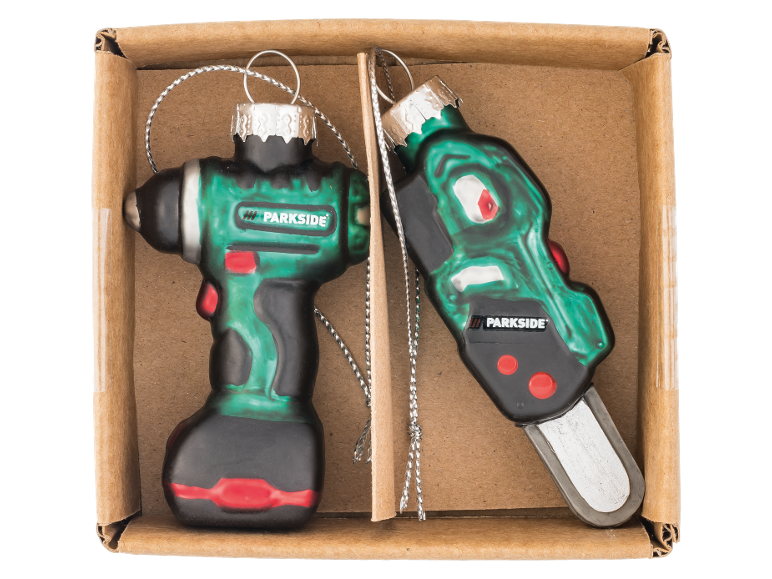 Dois ornamentos de Natal em forma de berbequim e motosserra numa caixa de cartão.