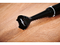 Liquidificador de imersão preto com lâmina de metal sobre uma superfície de madeira.
