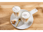 Dois copos de latte macchiato em camadas com leite espumado, biscoitos amaretti e uma colher.
